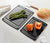 Up close detail of the All-in-One Cutting Board Set in Slate ready for meal prep with fresh asparagus and peppers ready to be expertly chopped with a Victorinox Swiss Modern Chef's knife with wood handle